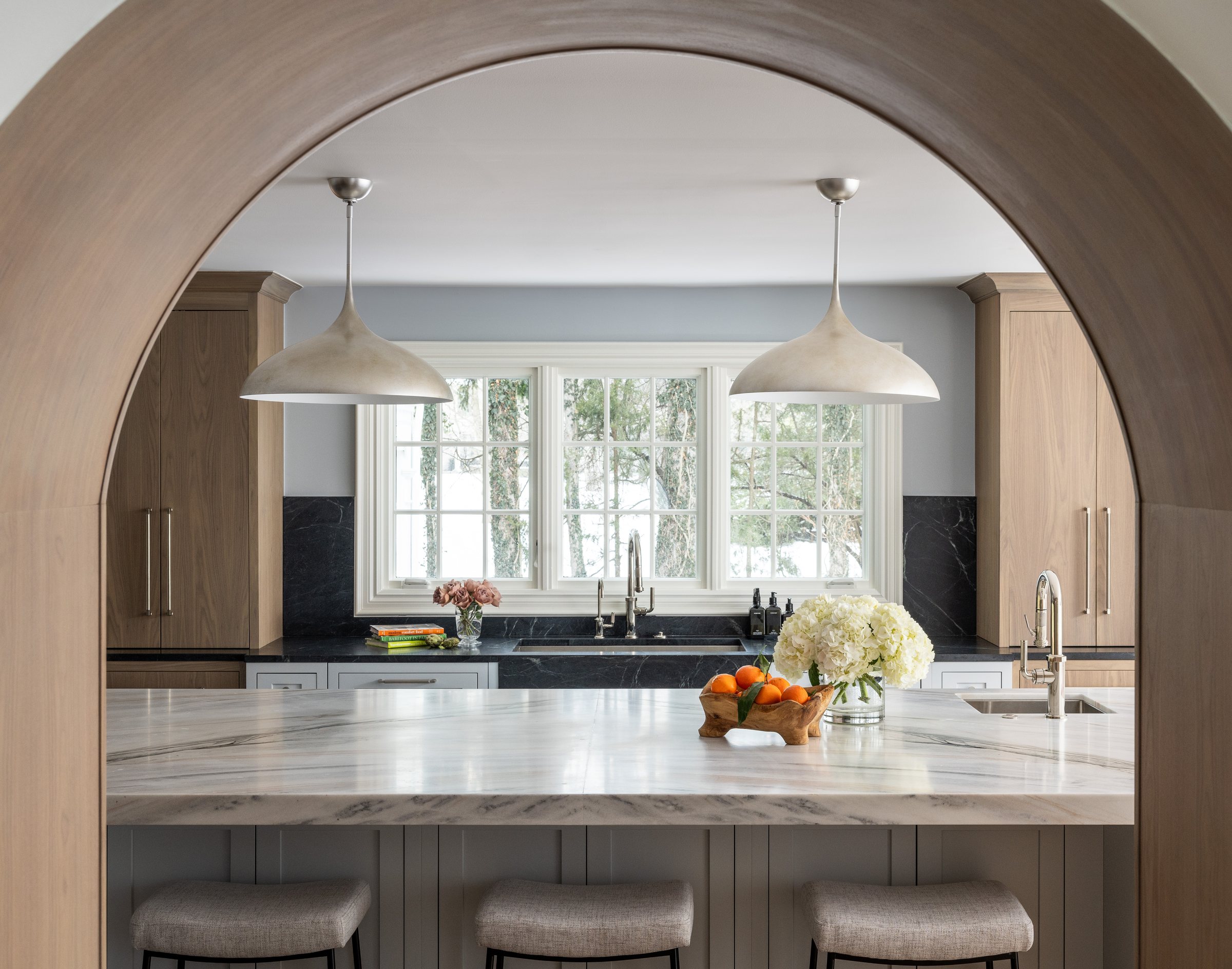 Kitchen with a marble island seen through a wide plaster arch