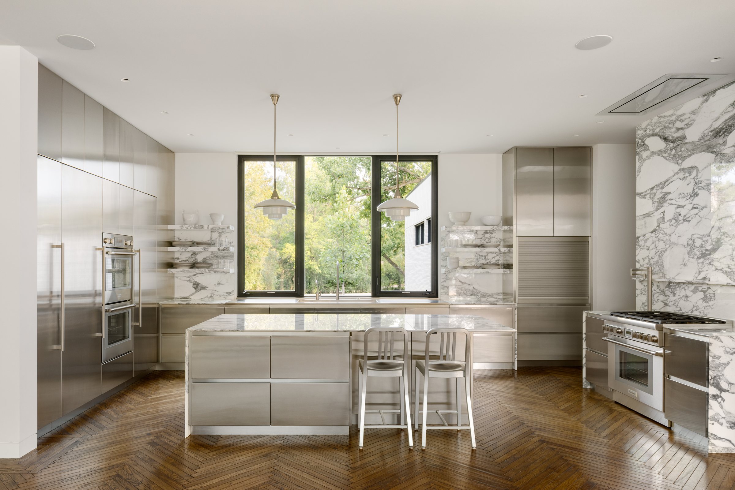 Kitchen in stainless steel and book-matched marble over herringbone oak, at Bluff House