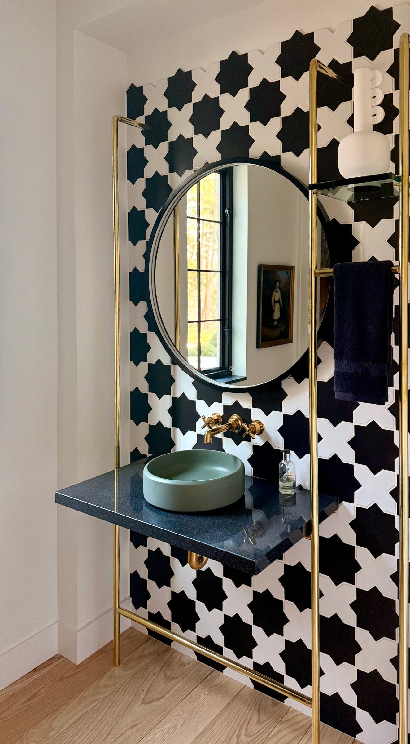 Powder room with a black-and-white star tile wall, brass stand, and a sage basin