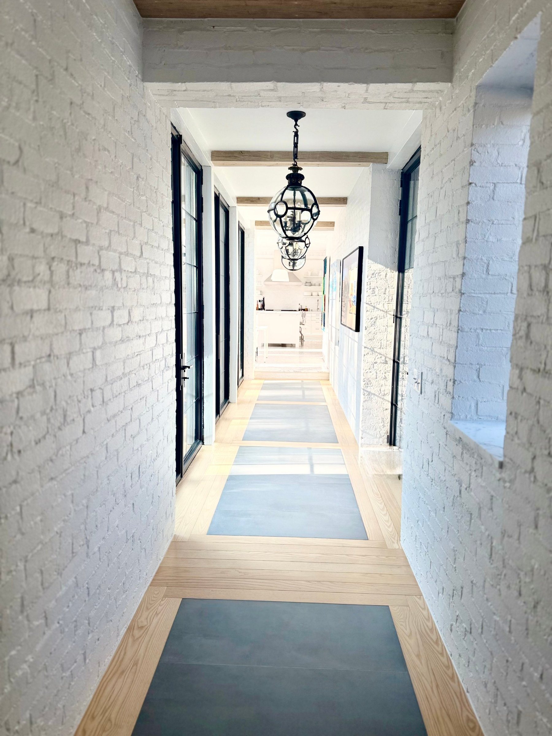 Hallway of white brick and steel-framed glass, with an ash hardwood floor and stone underfoot