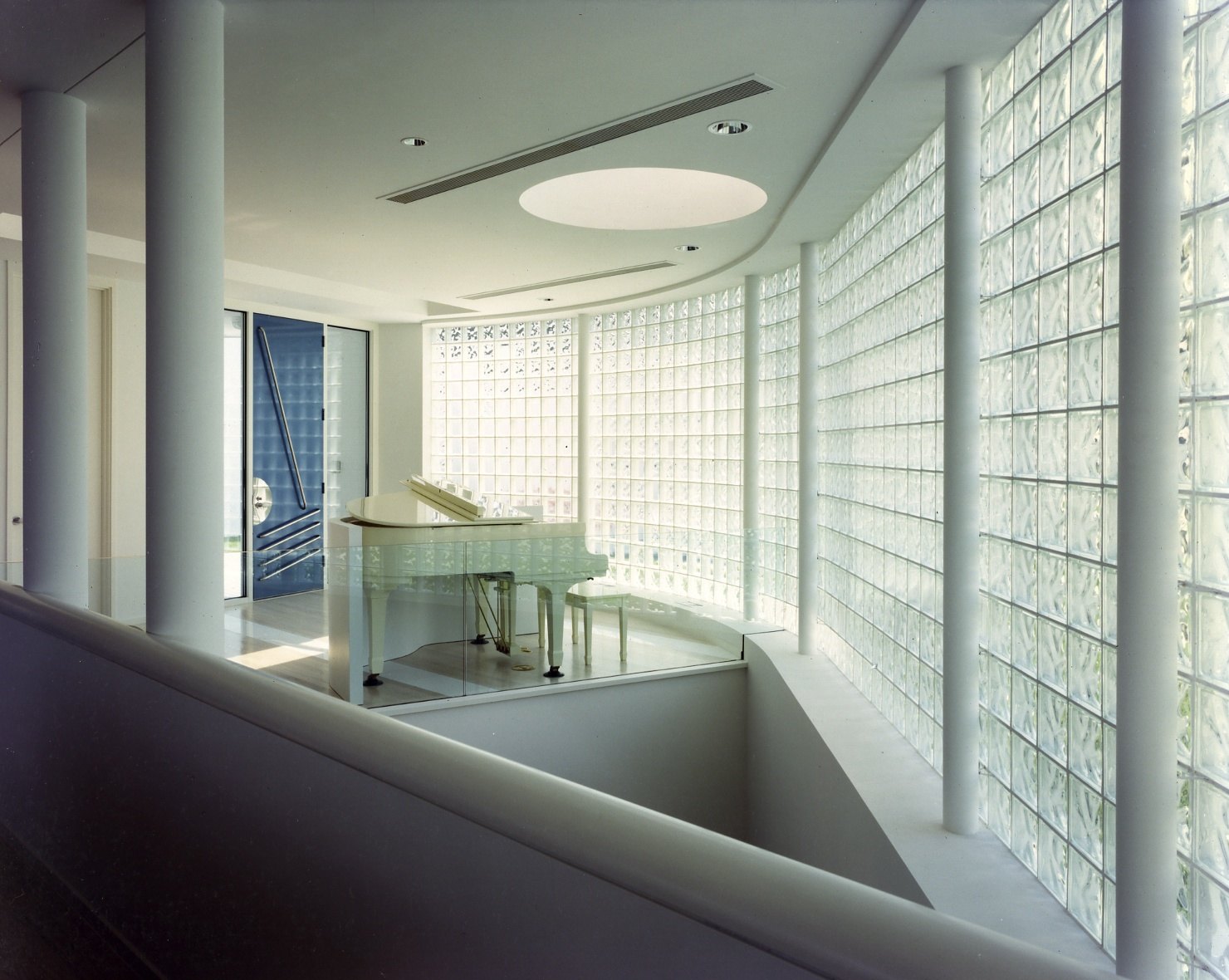 The piano on the upper landing against the curved glass-block wall