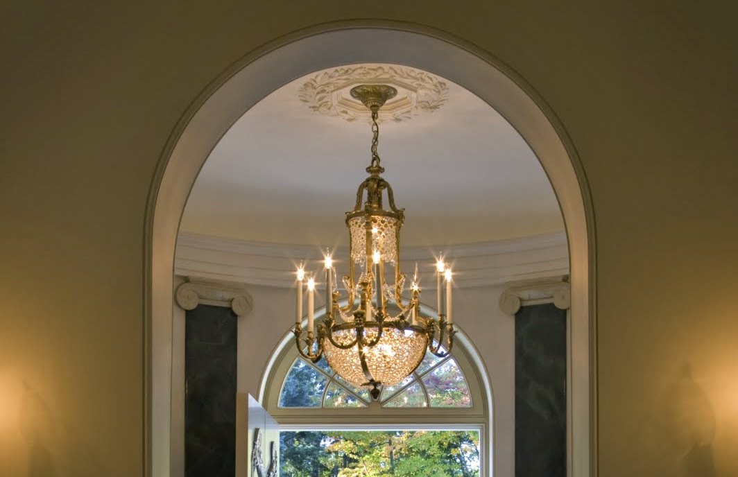 A crystal chandelier under a plaster medallion, seen through an arch