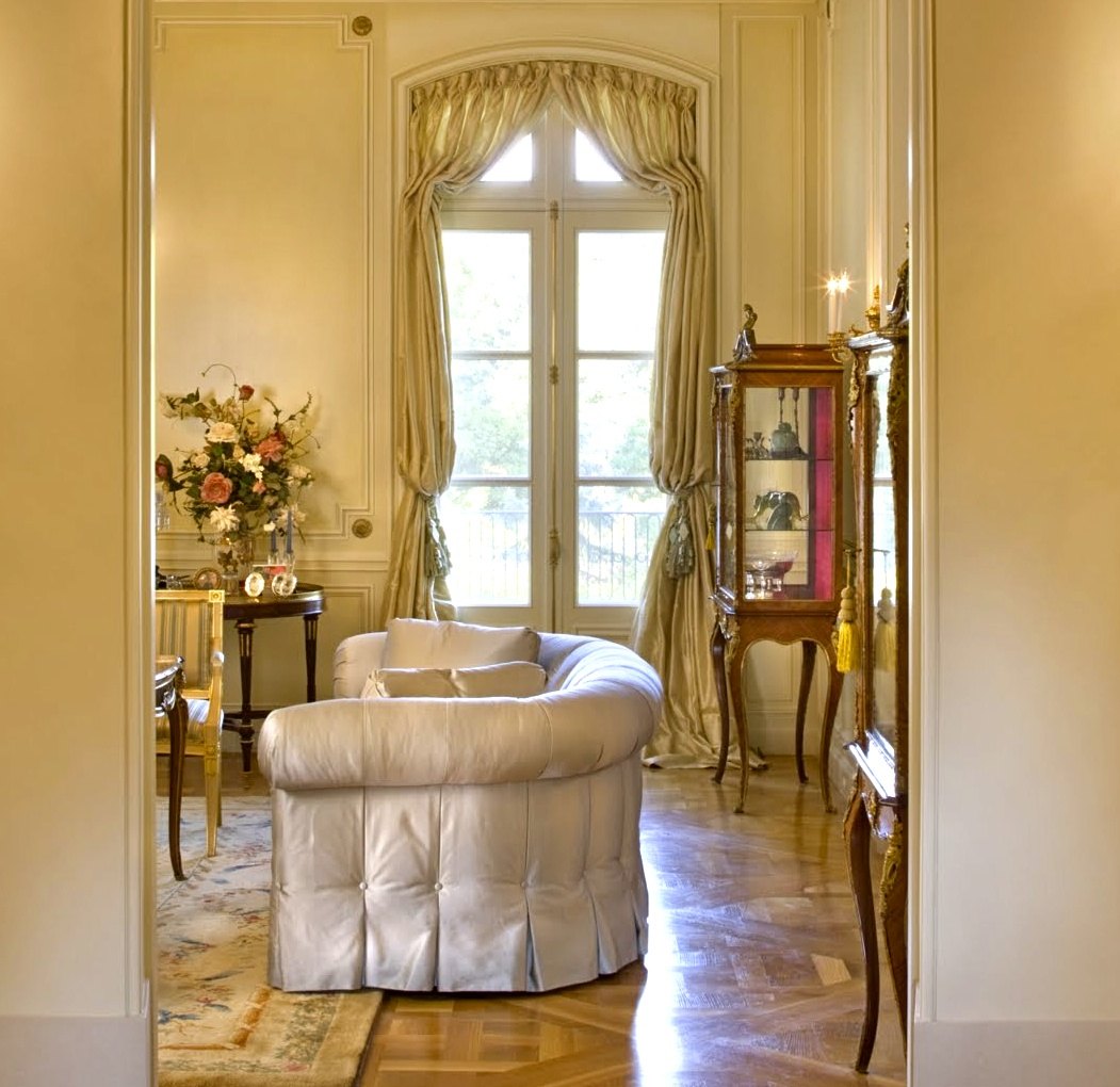The salon: paneled walls, silk curtains at the arched French doors, parquet de Versailles underfoot