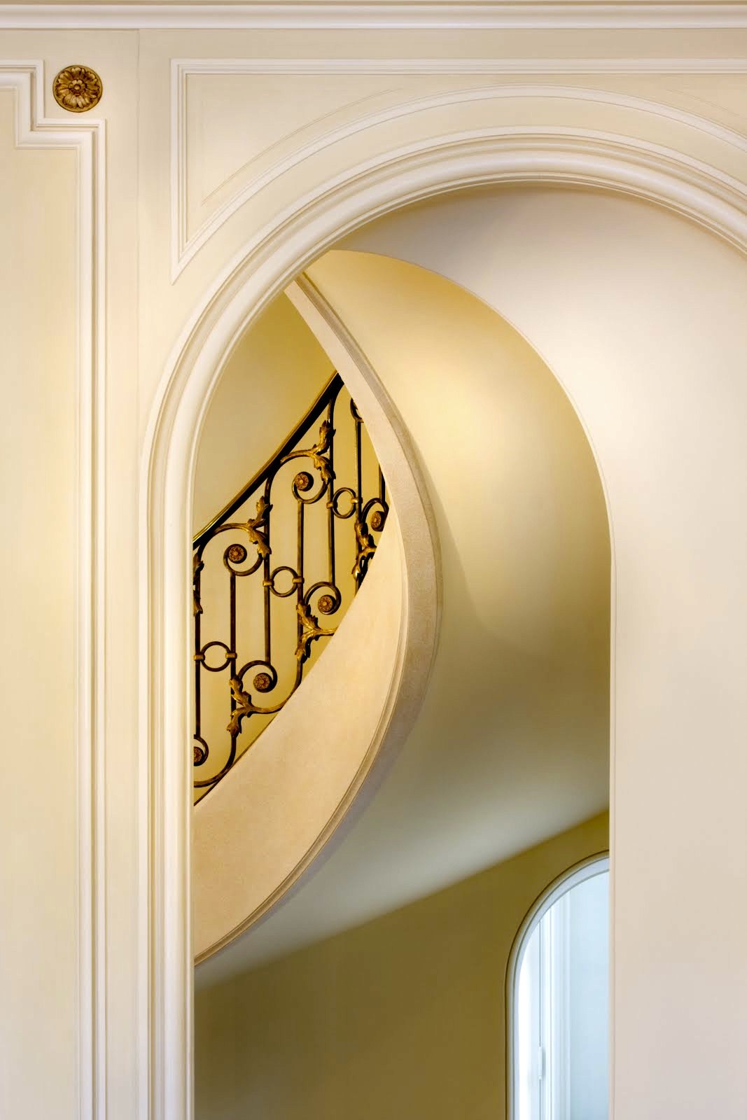 The curved stair and its iron railing, seen through an arched opening