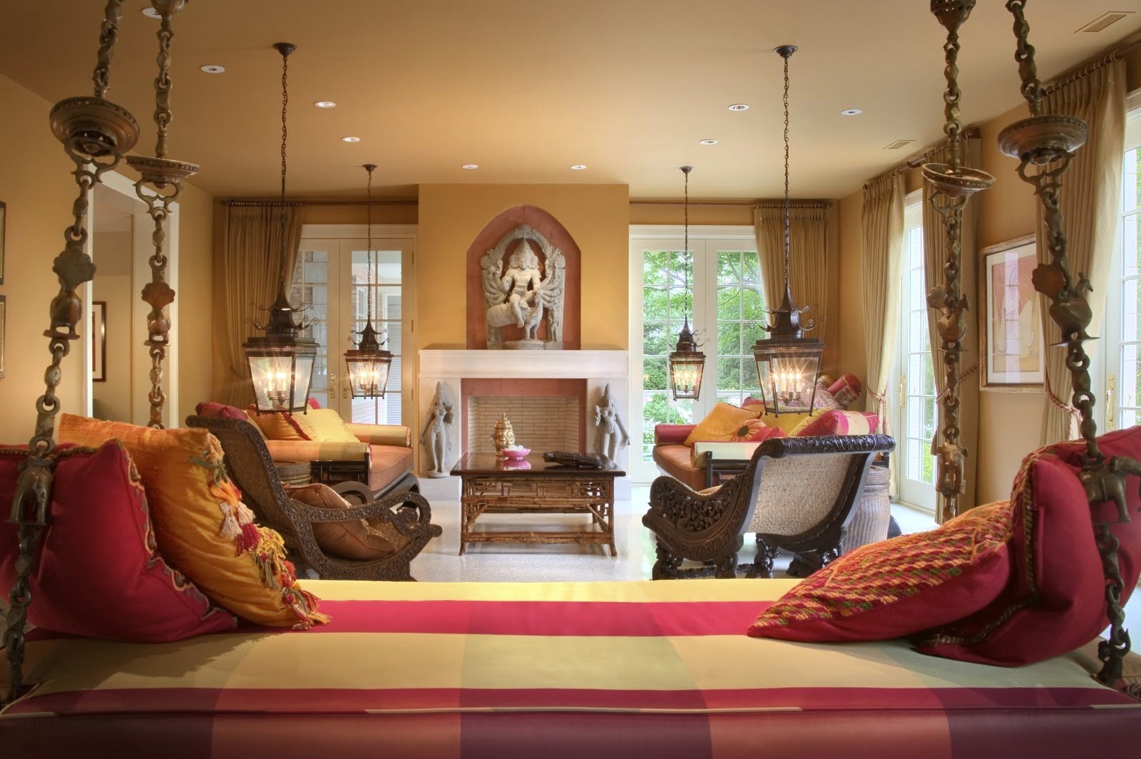 The living room: a hanging daybed, lanterns, carved chairs, and a stone deity above the fireplace