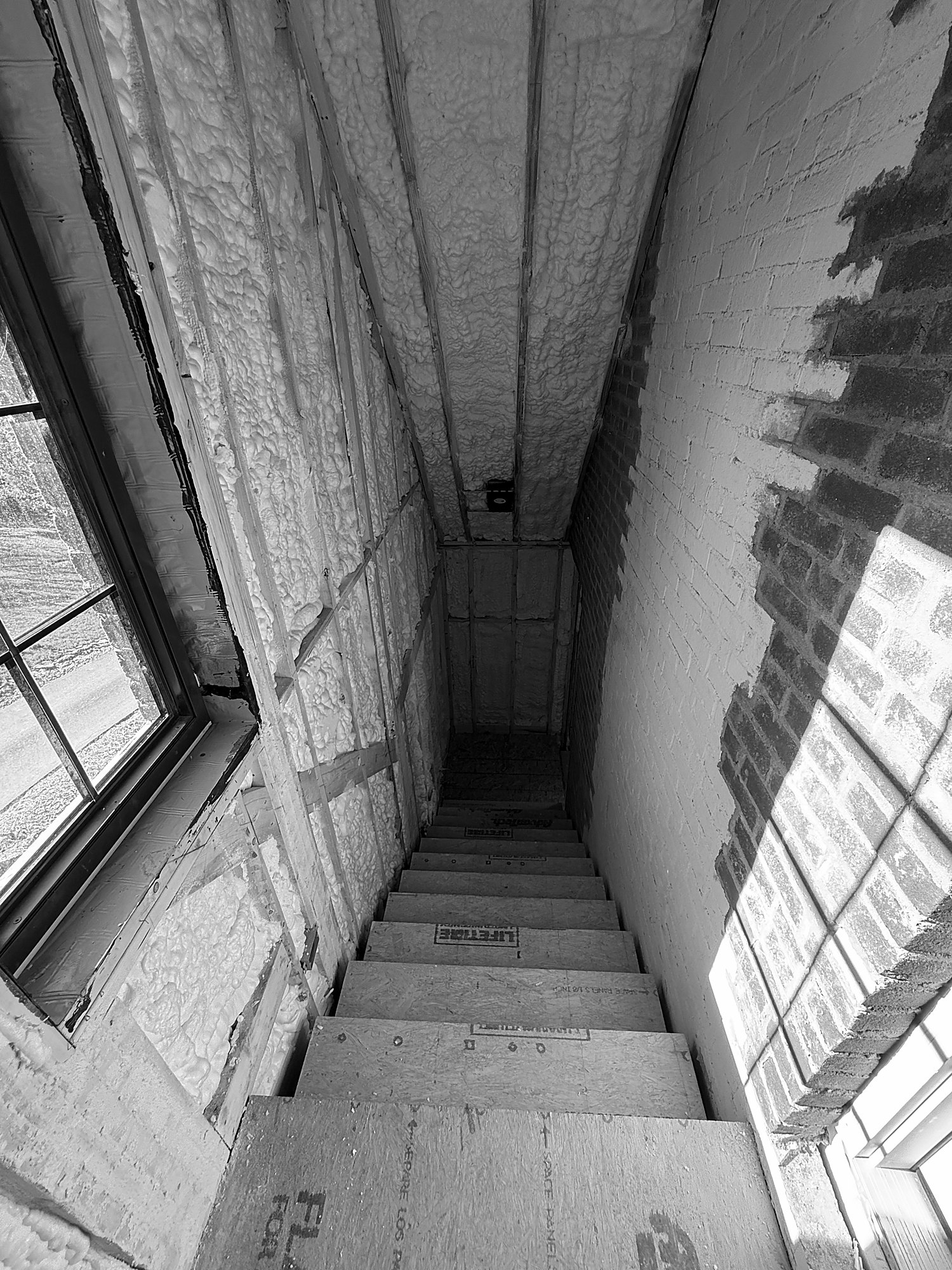 Spray foam carried tight to a window frame and across the walls and ceiling of a stair. The joint around each window is one of the places air barriers most often fail.