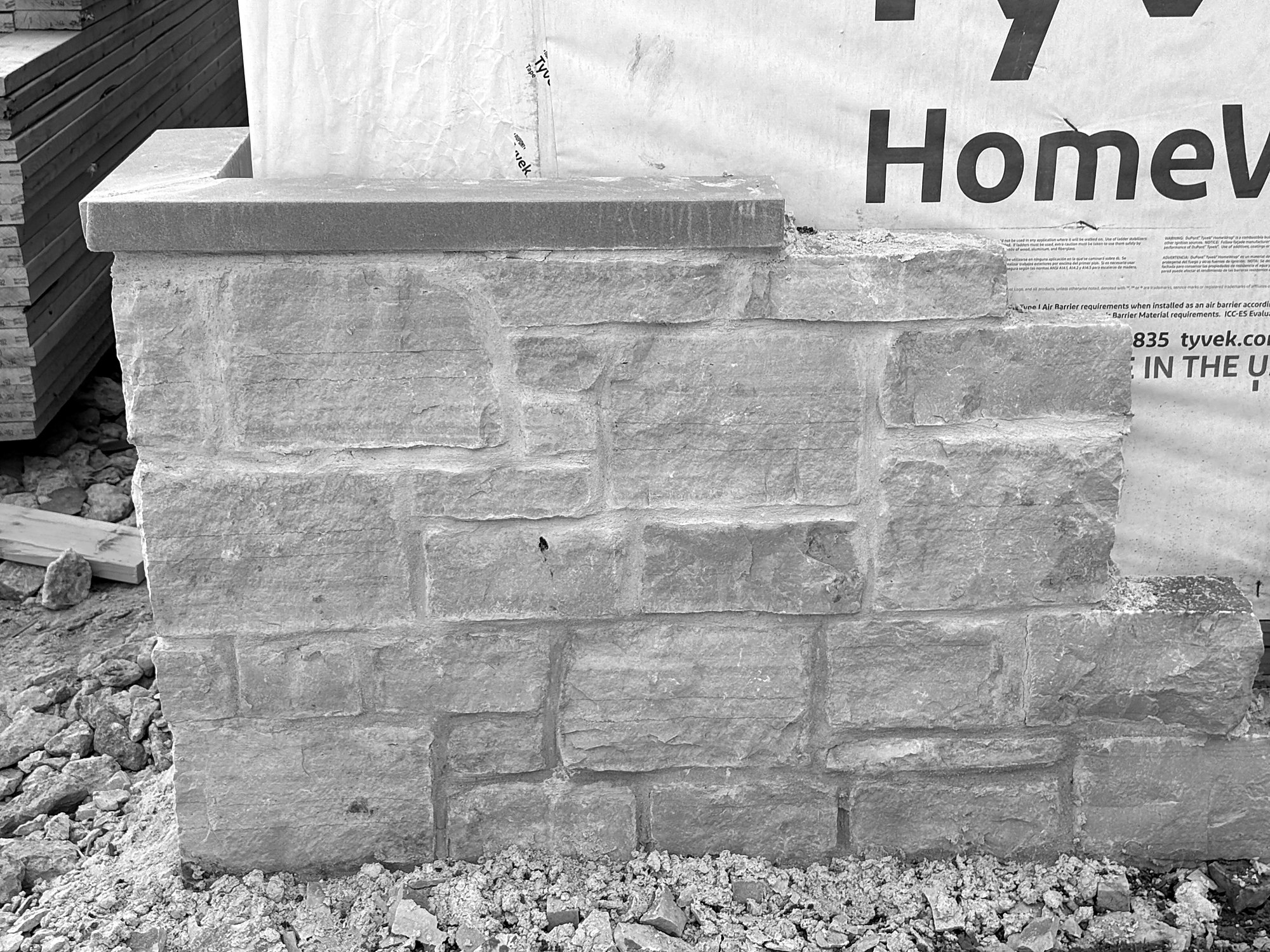 House wrap lapped down over a masonry mockup. The wrap is the drainage plane behind the cladding, the layer that turns water that gets past the stone back outside.