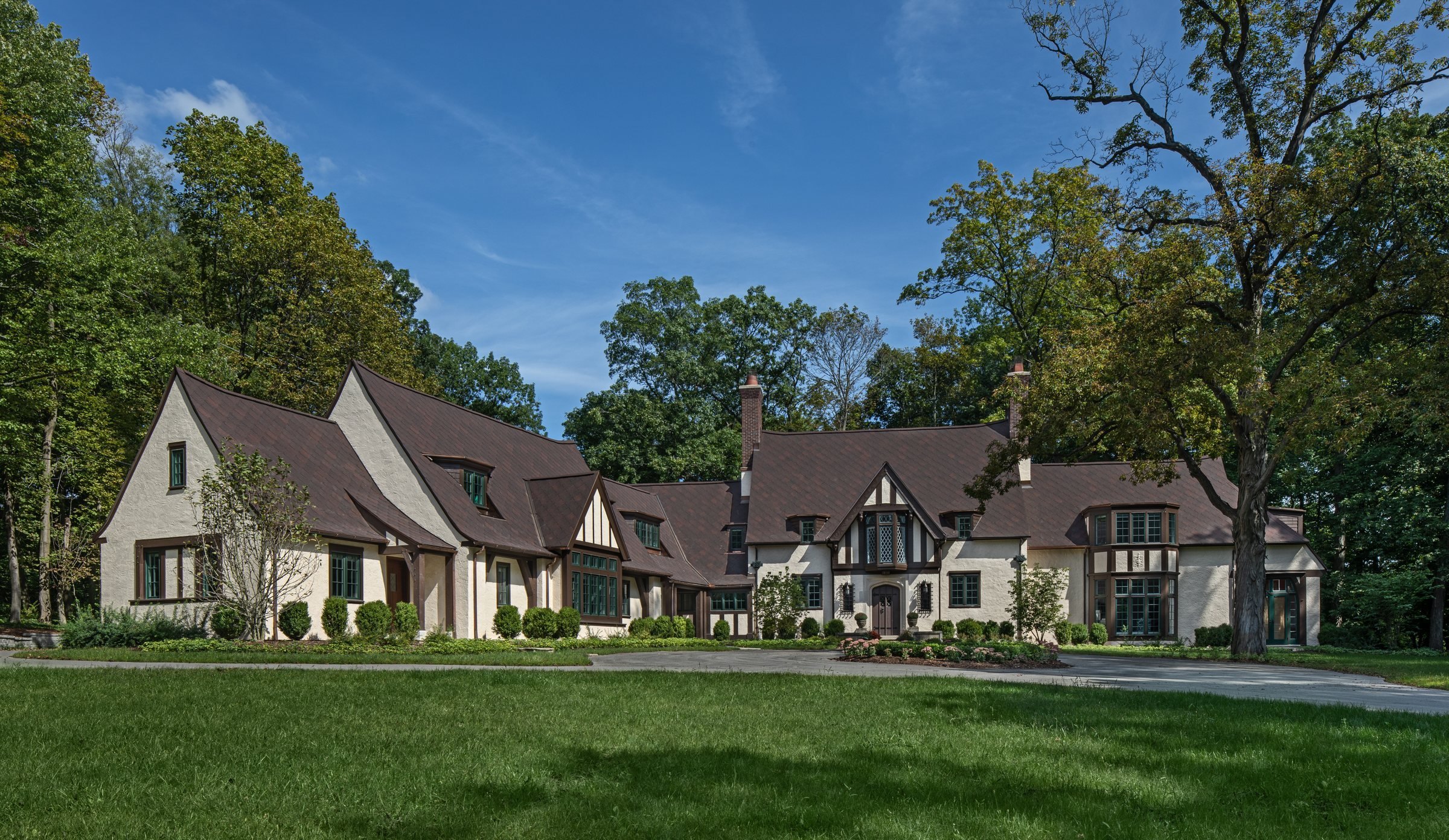 An English Tudor revival house across a broad lawn: half-timbered gables of different sizes, held together by a consistent steep roof pitch.