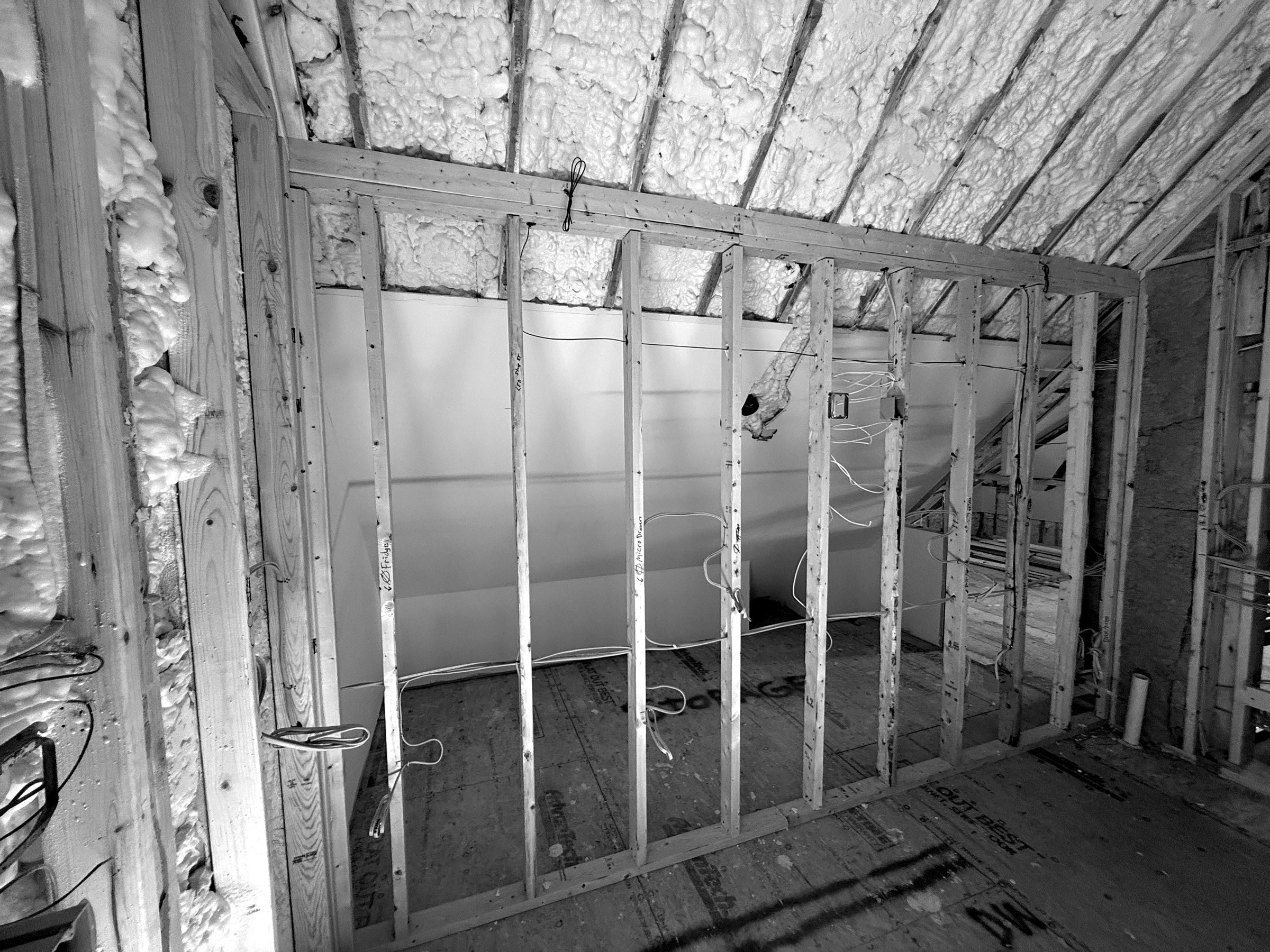 Spray foam applied between the rafters of a steep roof, with new partition framing in front. The attic space behind becomes part of the conditioned house.