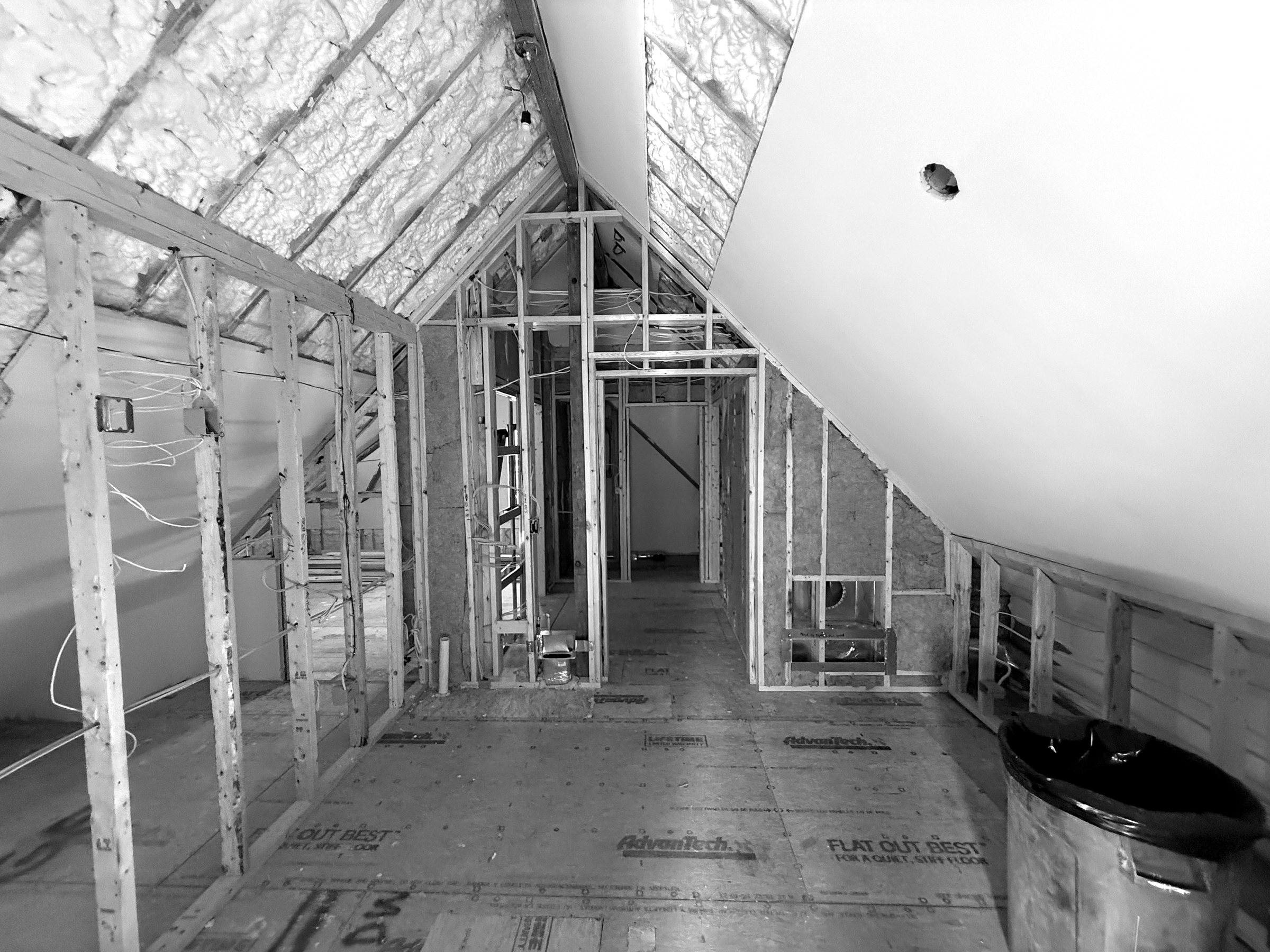 An attic room before drywall: foam across the sloped ceiling and knee walls, framing and rough wiring in place.