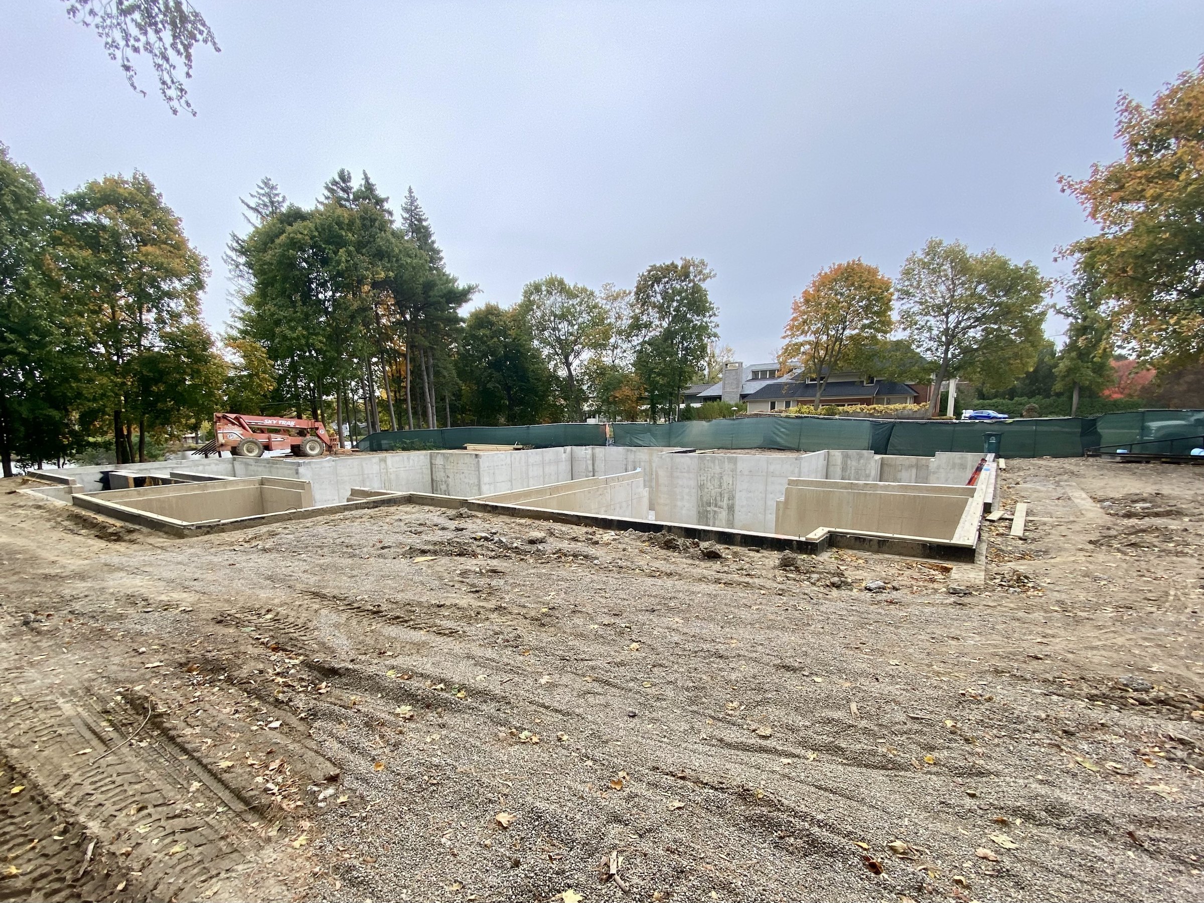 Poured foundation walls on a cleared lot under autumn trees